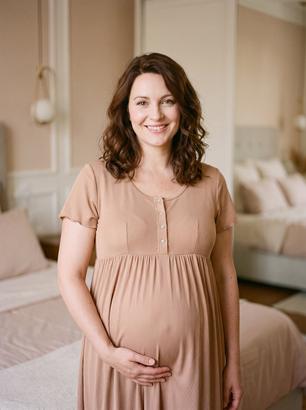 Femme enceinte en chemise de nuit de grossesse rose poudré, debout dans une chambre