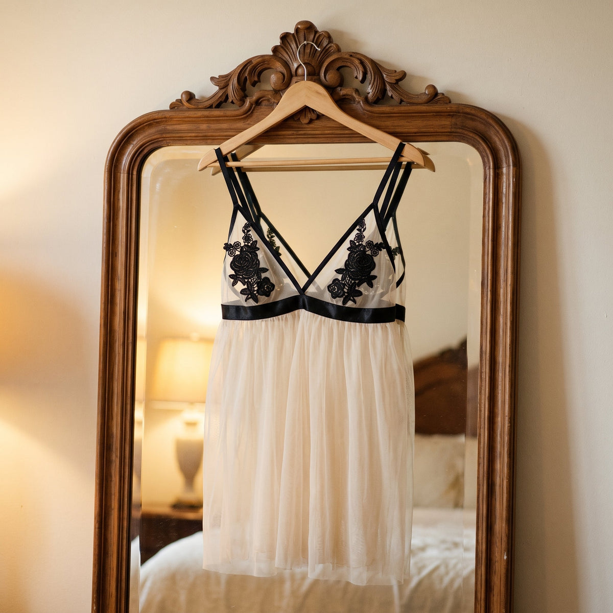 La nuisette suspendue à un cintre devant le grand miroir de la chambre, ses courbes dessinées par le voile clair et la lumière chaude d’une lampe renvoyée par la glace