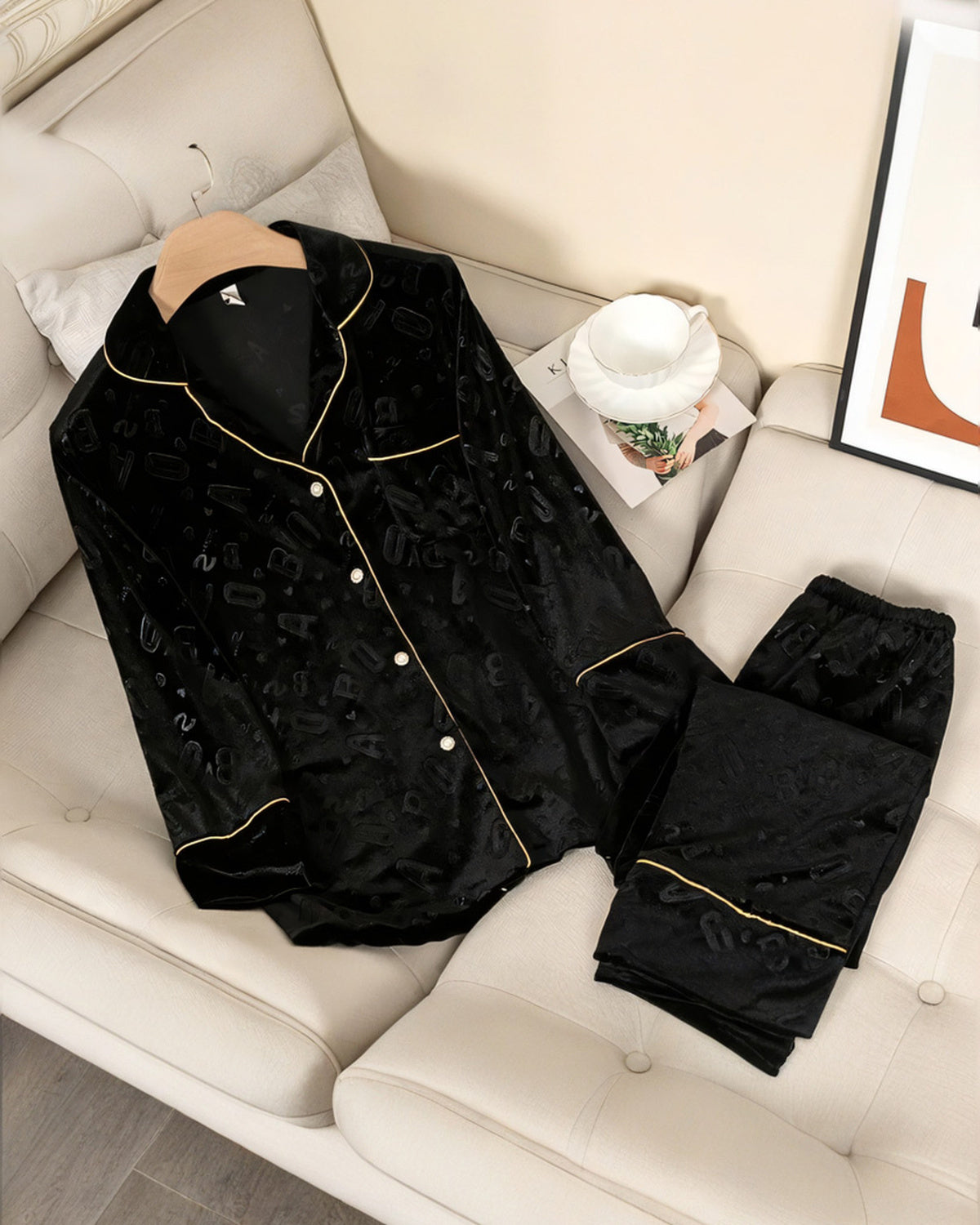 Ensemble de pyjama en velours noir à lettres en relief, chemise et pantalon posés sur un canapé crème