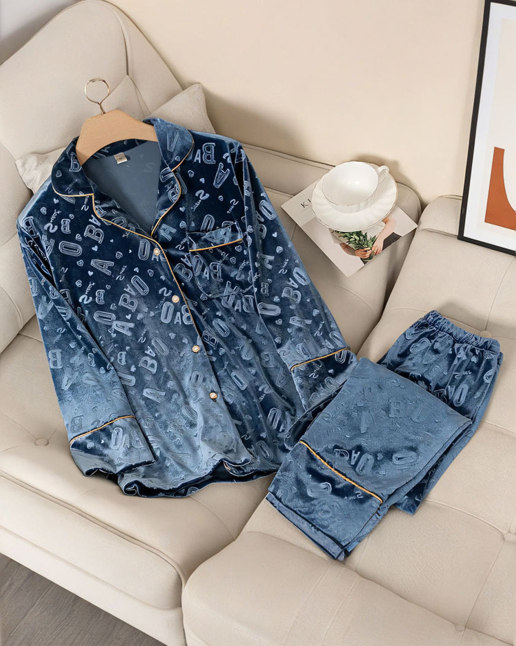 Ensemble de pyjama en velours bleu à lettres en relief, chemise et pantalon posés sur un canapé crème