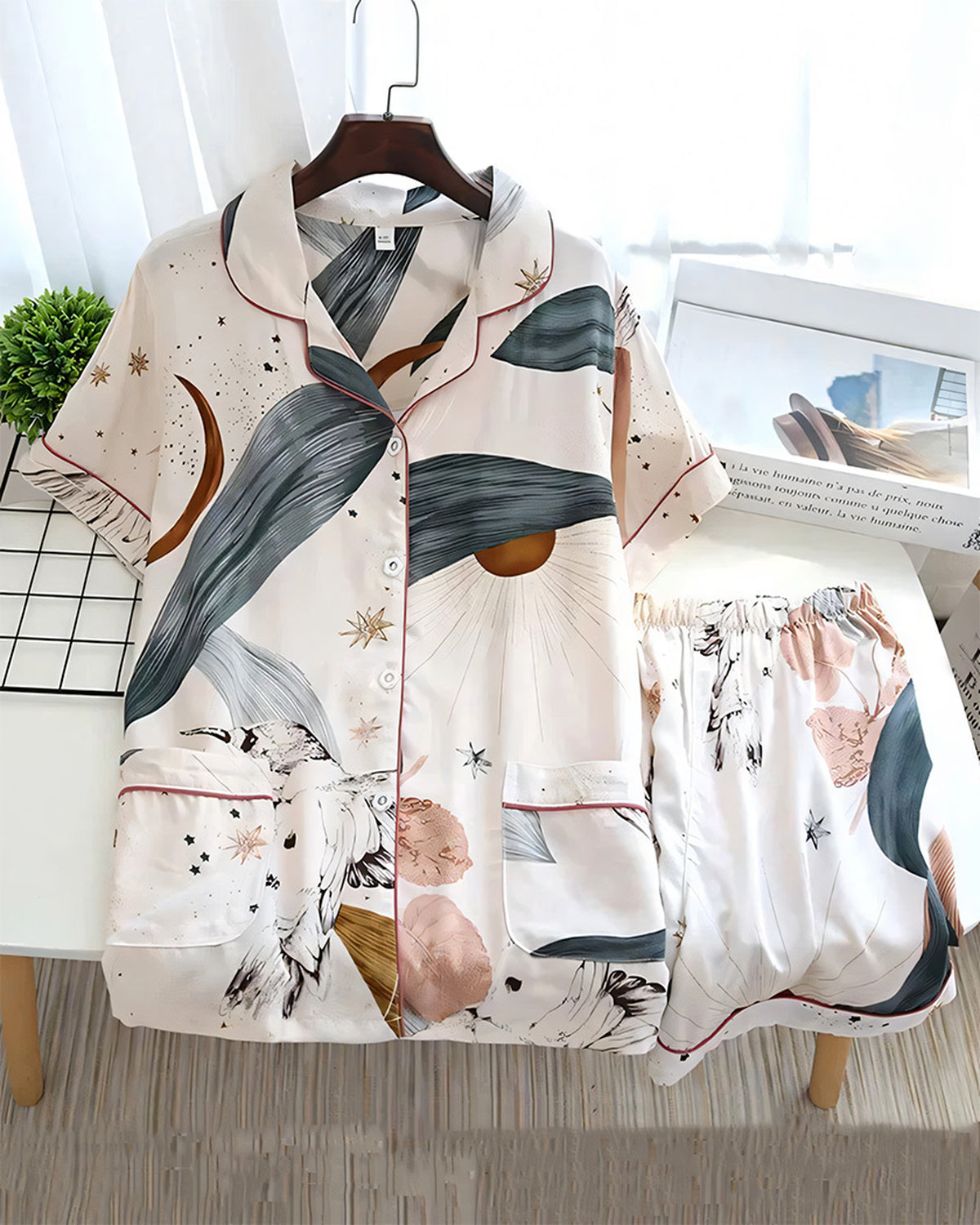 Chemise de pyjama crème sur un cintre et son short posé à côté, imprimé d'astres dorés et de coups de pinceau gris