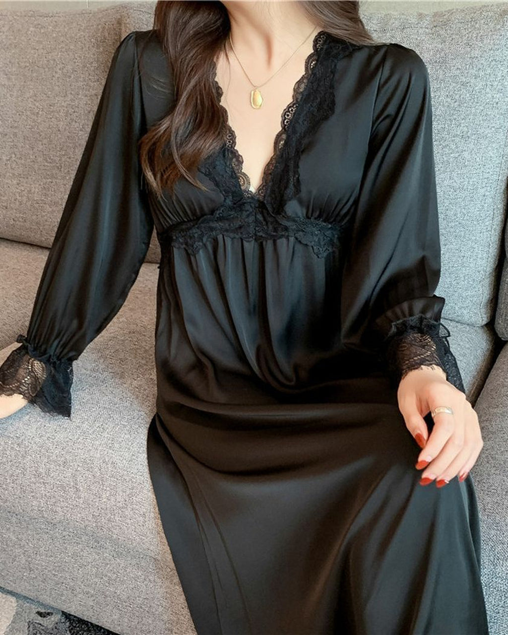 Nuisette longue en satin noir portée assise, décolleté en V à dentelle