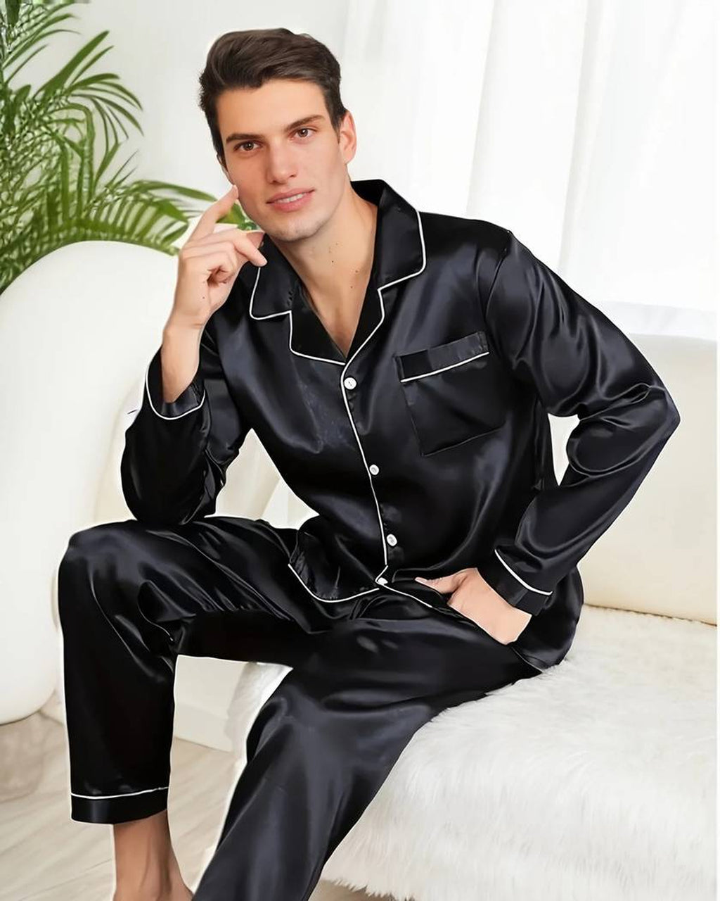 Homme assis en pyjama deux pièces noir satiné, chemise boutonnée à col cranté et liseré blanc, près d'une fenêtre voilée