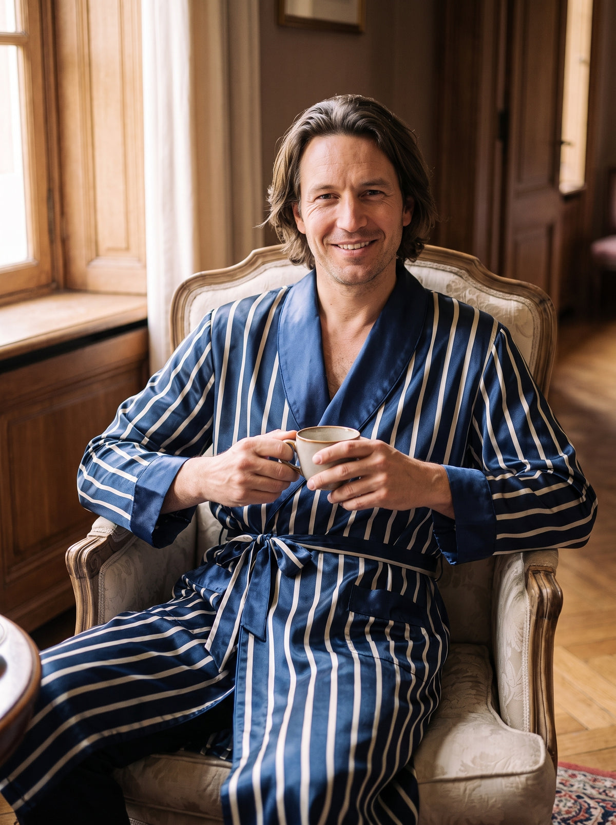Robe de chambre homme satin bleu marine portée dans un fauteuil, ambiance raffinée