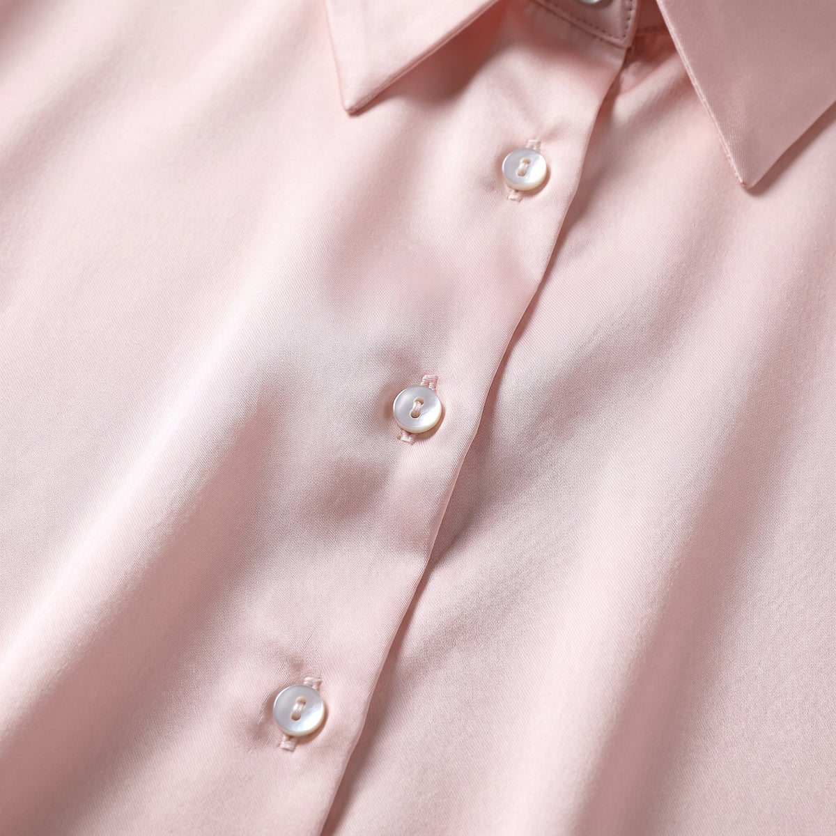 Détail des boutons nacrés et du col chemise sur le satin rose poudré