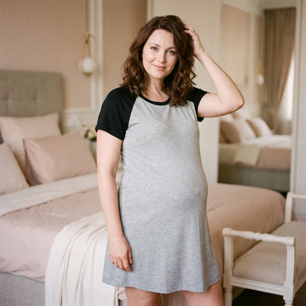 Femme enceinte debout devant une fenêtre en chemise de nuit gris chiné, col rond bordé de noir
