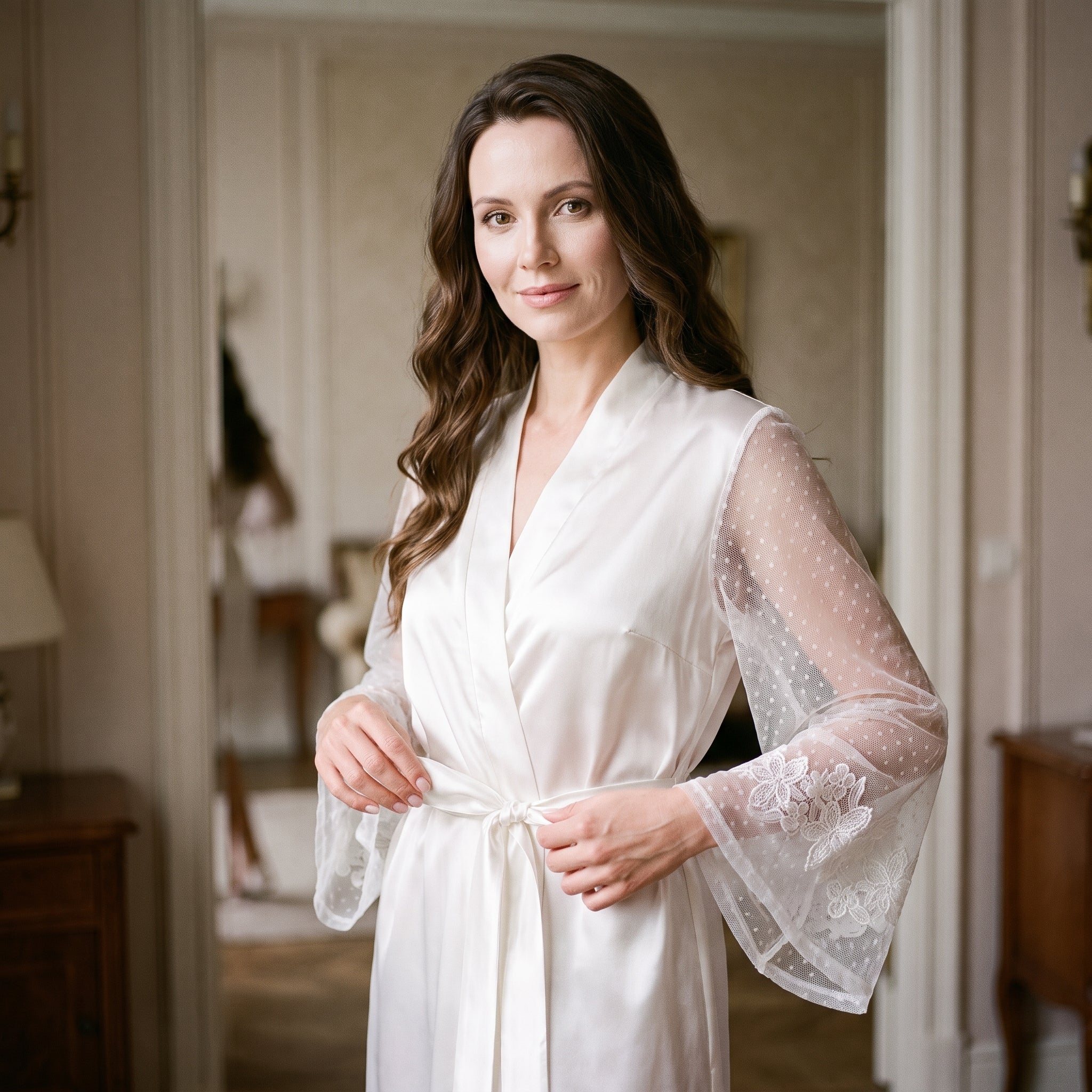 Elle noue la ceinture de satin devant le grand miroir de la chambre, le peignoir blanc posé sur les épaules Image