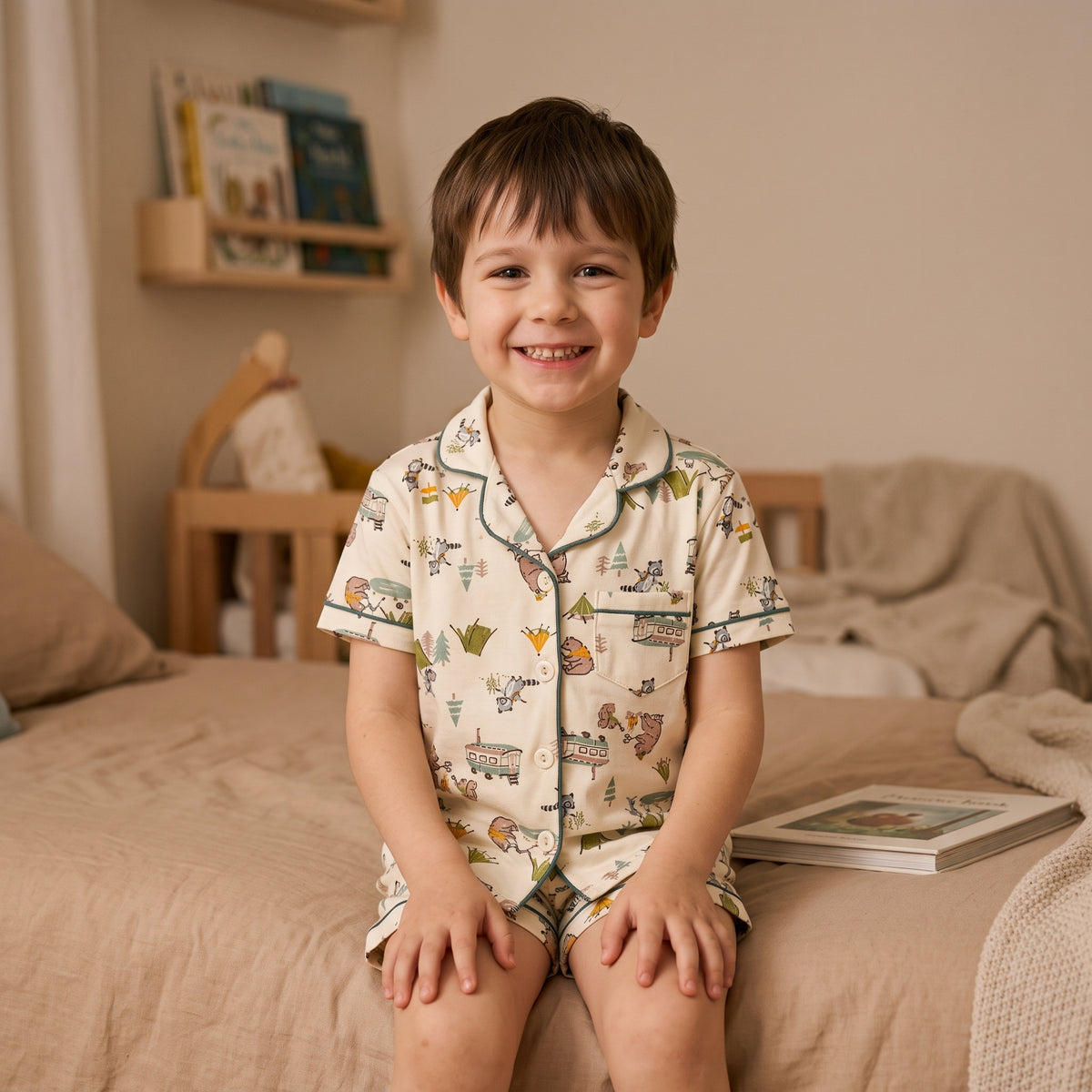 Garçon souriant assis sur son lit en pyjama court imprimé avant l’histoire du soir