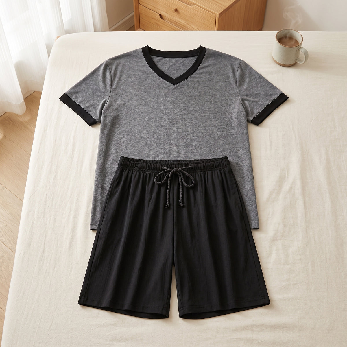 Ensemble de pyjama homme posé à plat sur un lit au matin, tee-shirt gris à encolure en V et short noir à cordon noué