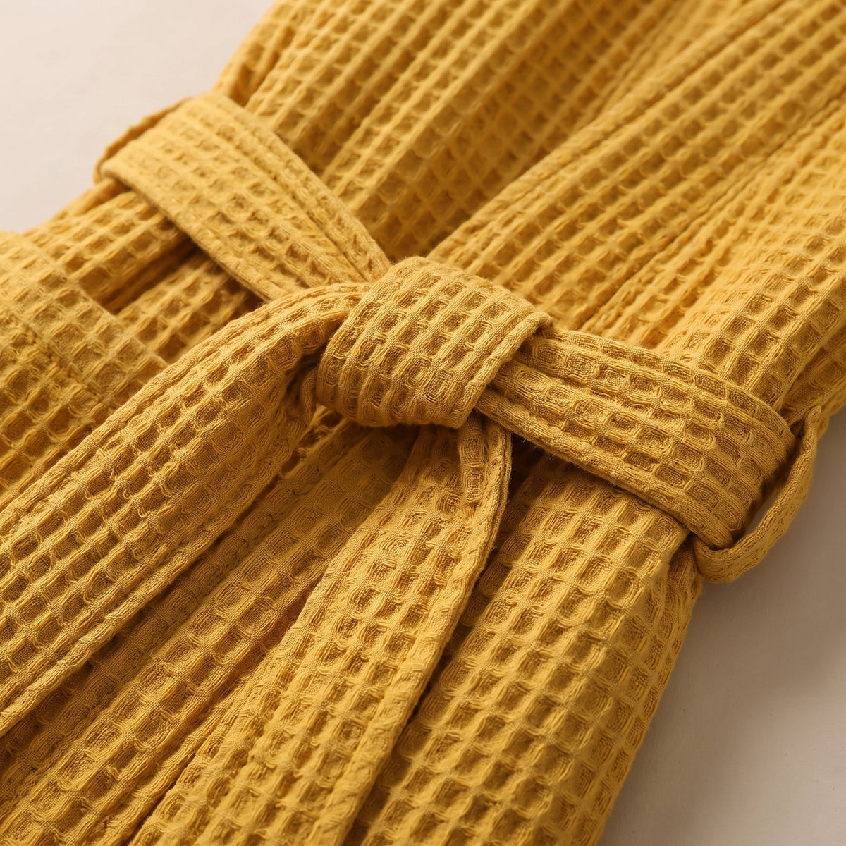 Détail de la ceinture nouée et de son passant sur le peignoir gaufré jaune moutarde