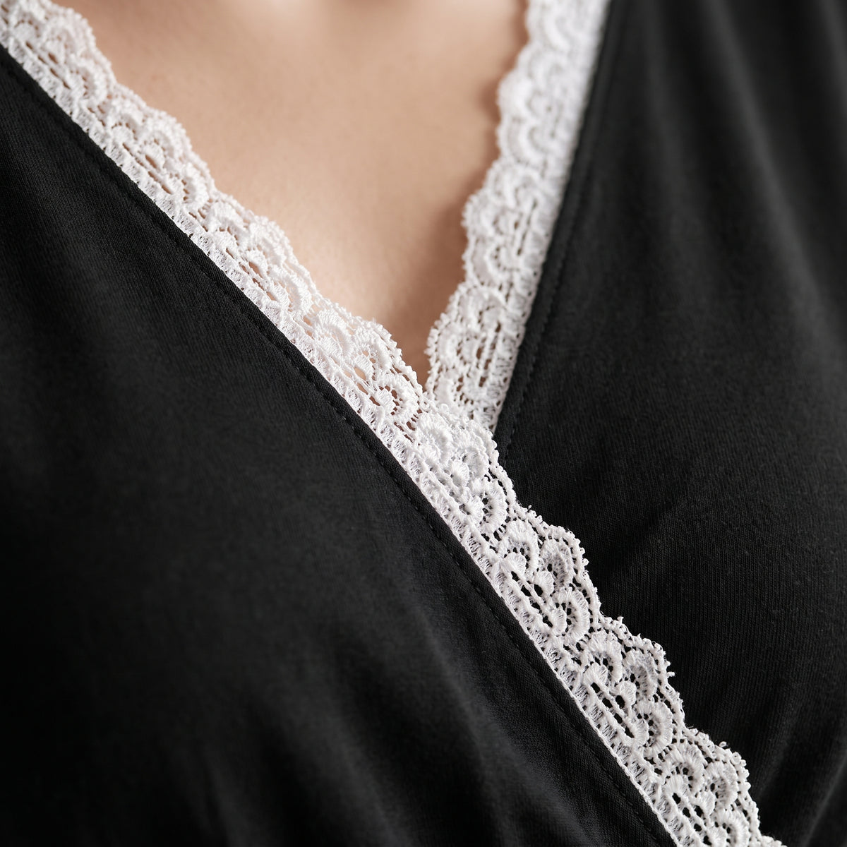 Gros plan sur le devant croisé et la dentelle blanche de la nuisette de maternité noire