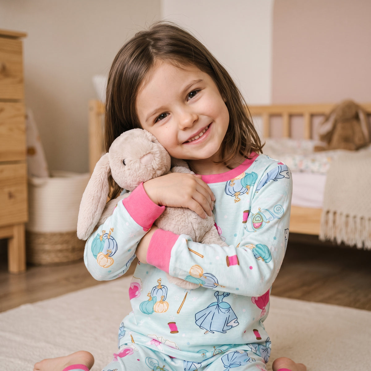 Petite fille assise sur le tapis de sa chambre, une peluche serrée contre elle, douceur du pyjama à poignets roses