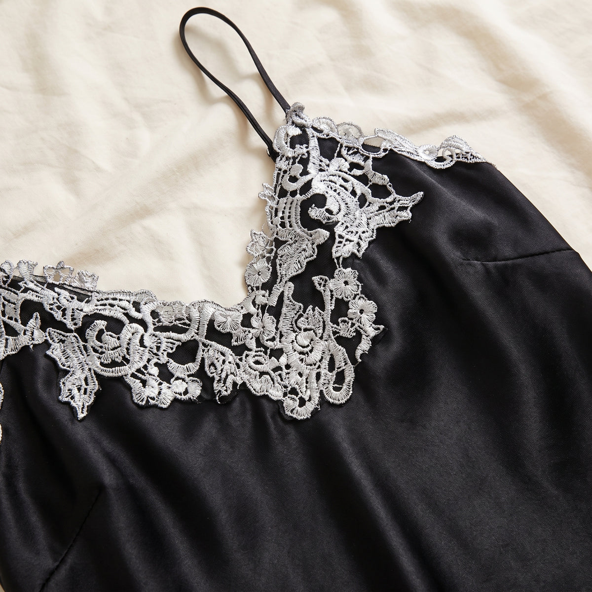 Dentelle argentée à volutes vue de près sur le satin noir de l’encolure