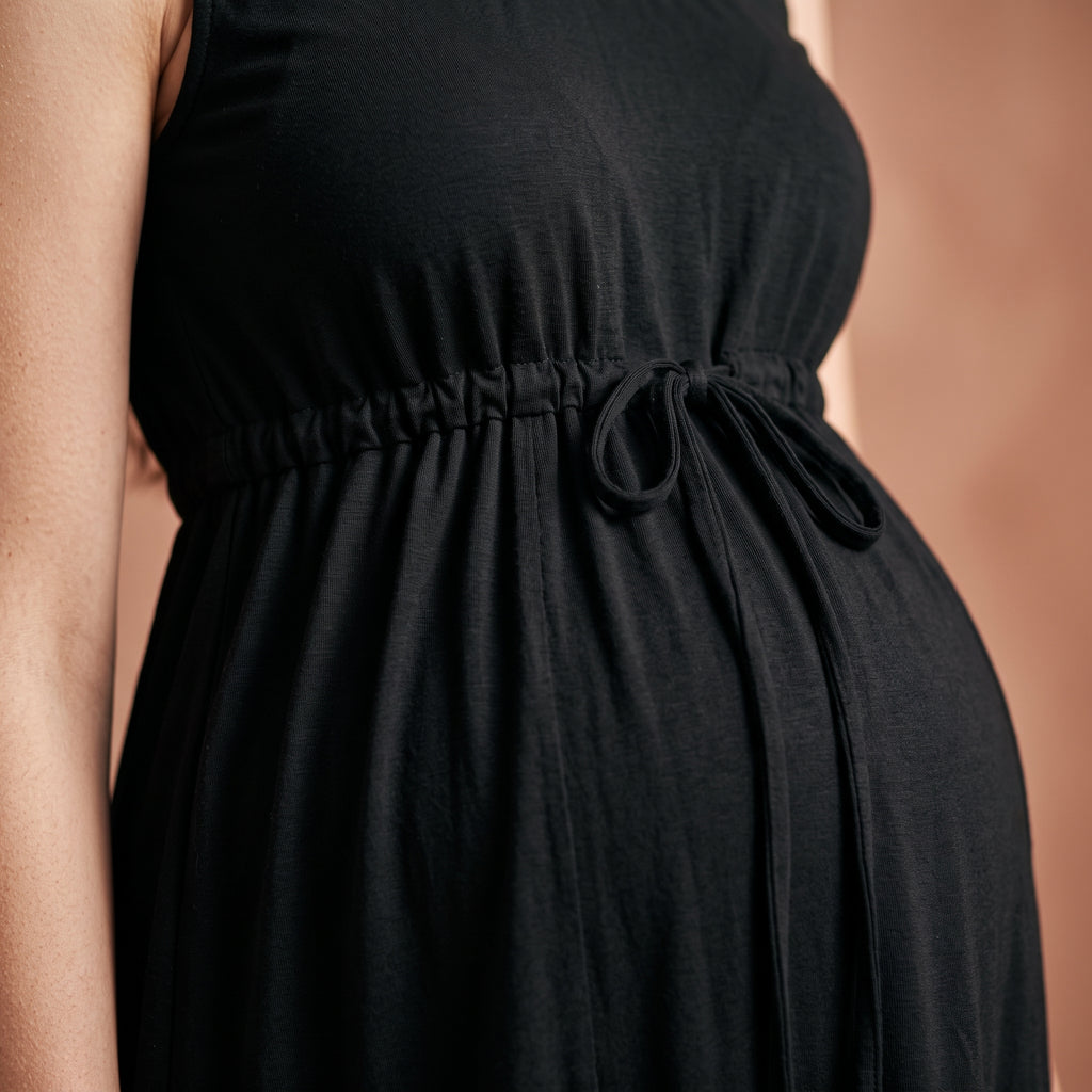 Gros plan sur le cordon noué à la taille de la nuisette de maternité noire, porté sur un ventre arrondi