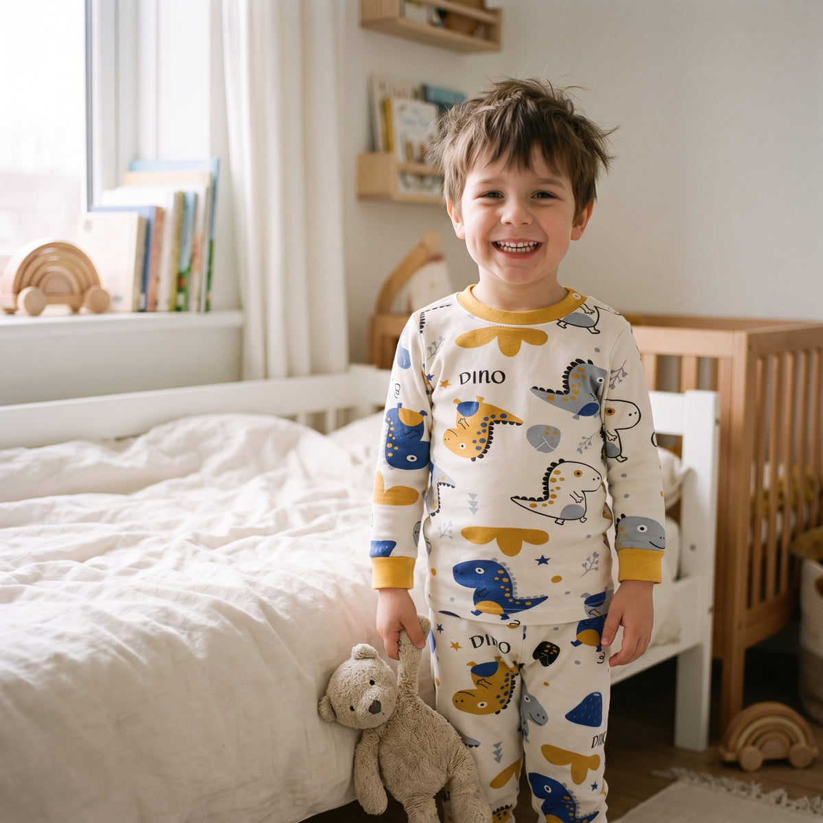 Petit garçon au réveil en pyjama dinosaures, son doudou à la main, devant son lit