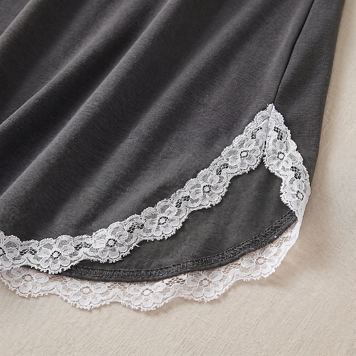 Détail de l'ourlet arrondi à liseré de dentelle blanche et de la fente latérale