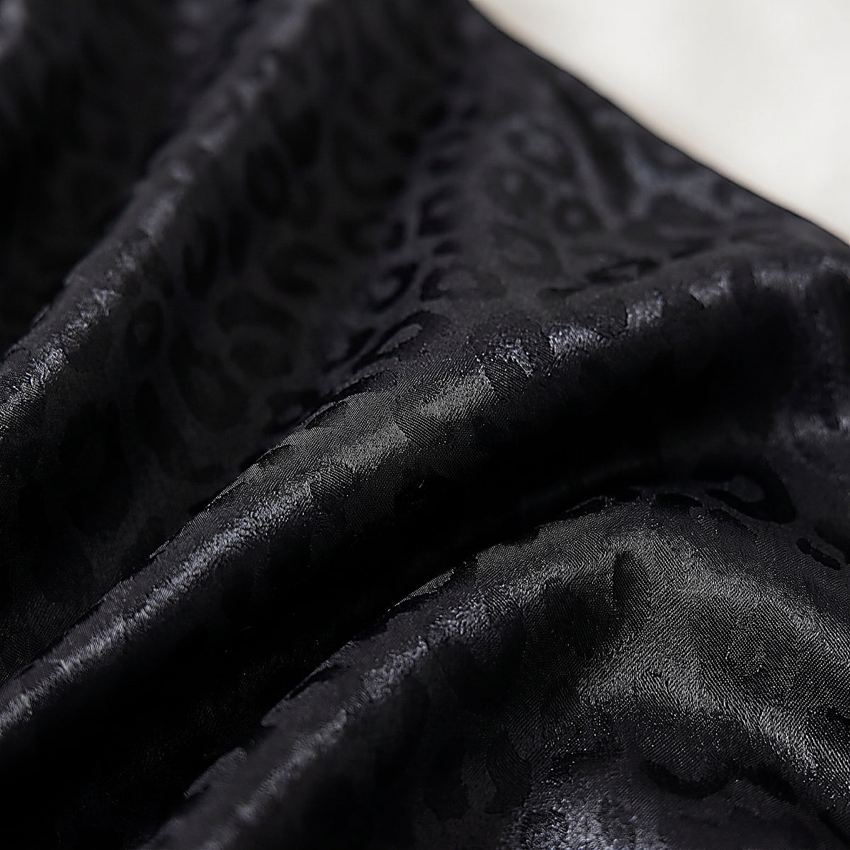 Détail du motif léopard ton sur ton du satin noir du pyjama