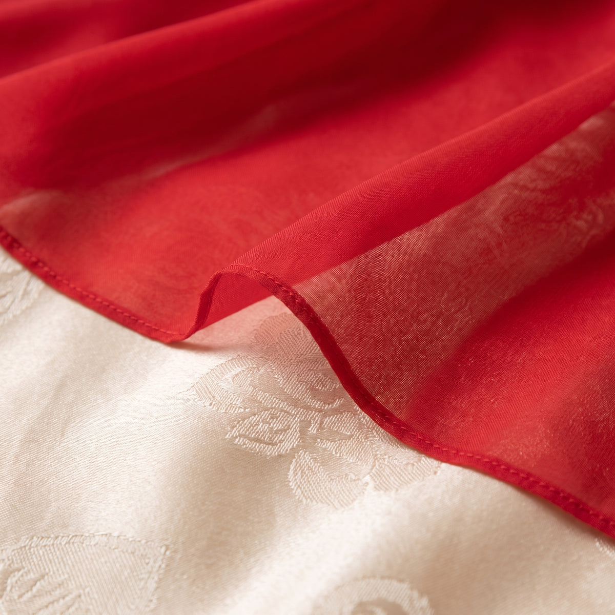 Macro du voile de satin rouge translucide de la jupe, posé sur un drap ivoire