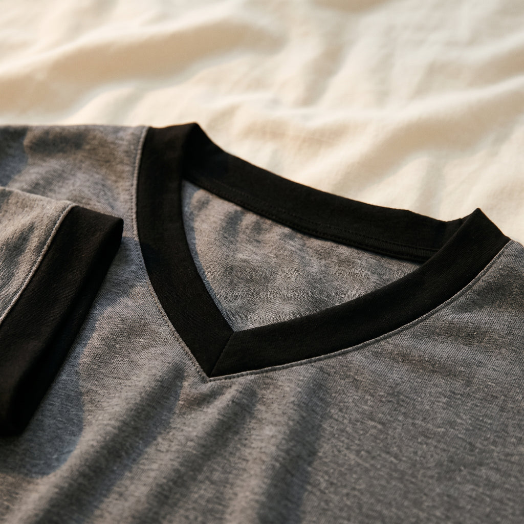 Gros plan sur l'encolure en V d'un tee-shirt de pyjama gris, bordée d'une large bande noire qui se rejoint en pointe