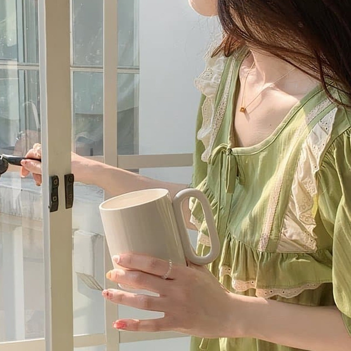 Modele ouvrant une fenetre en portant la nuisette verte en coton, lumiere naturelle