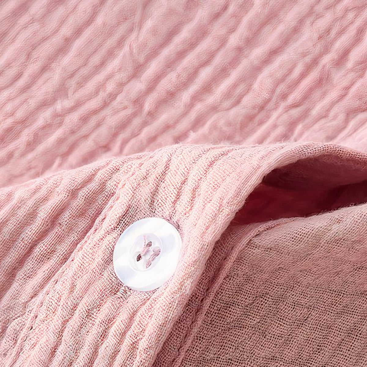 Gros plan du coton froissé rose et d'un bouton nacré de la robe de chambre Image
