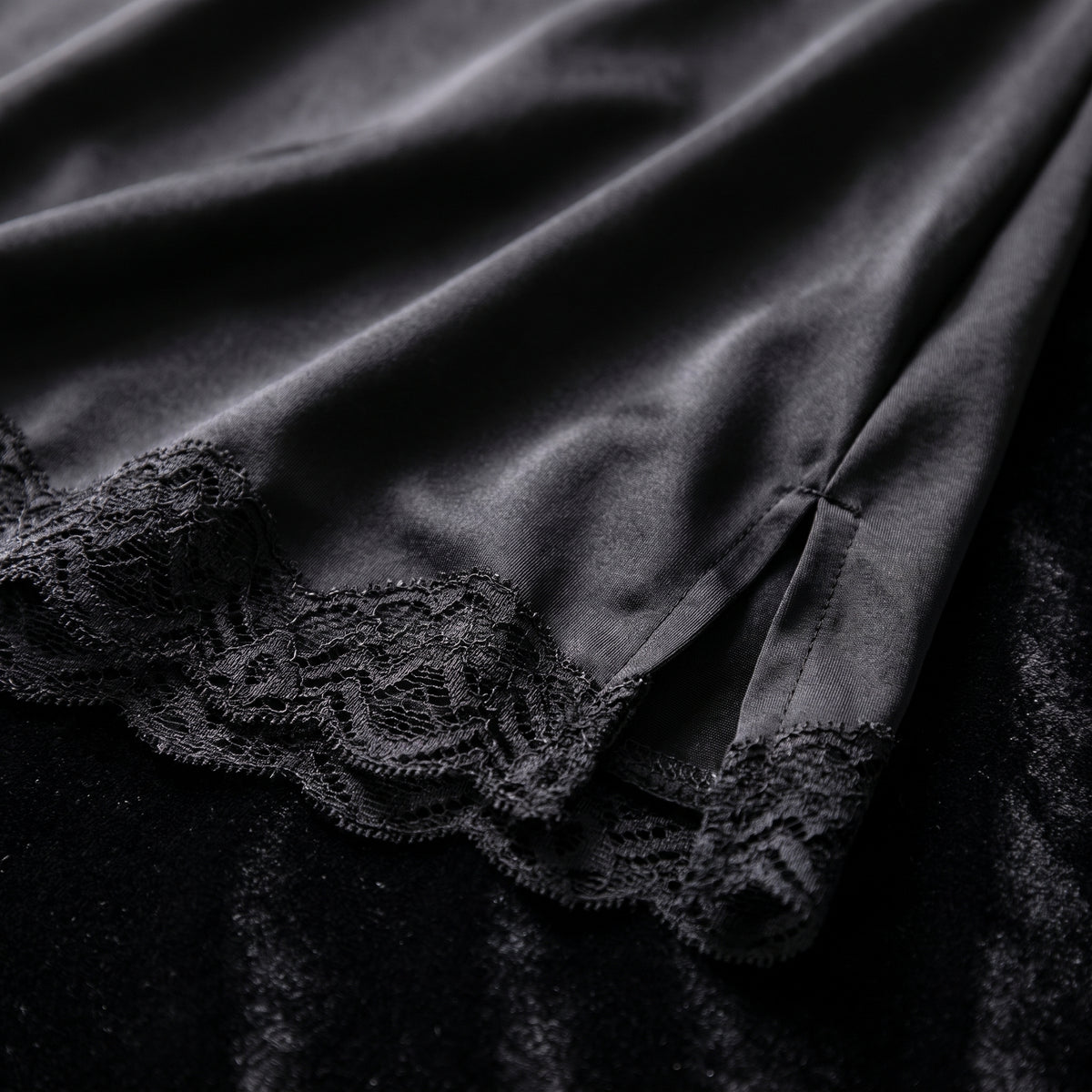 Détail de l'ourlet en satin noir bordé de dentelle festonnée et de la fente