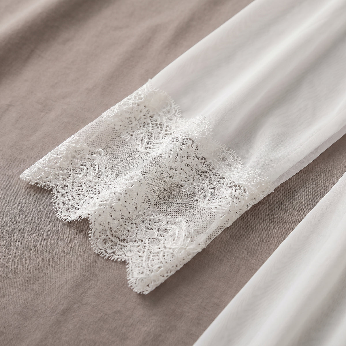 Détail de la manche en voile bordée de dentelle ajourée de la sur-robe
