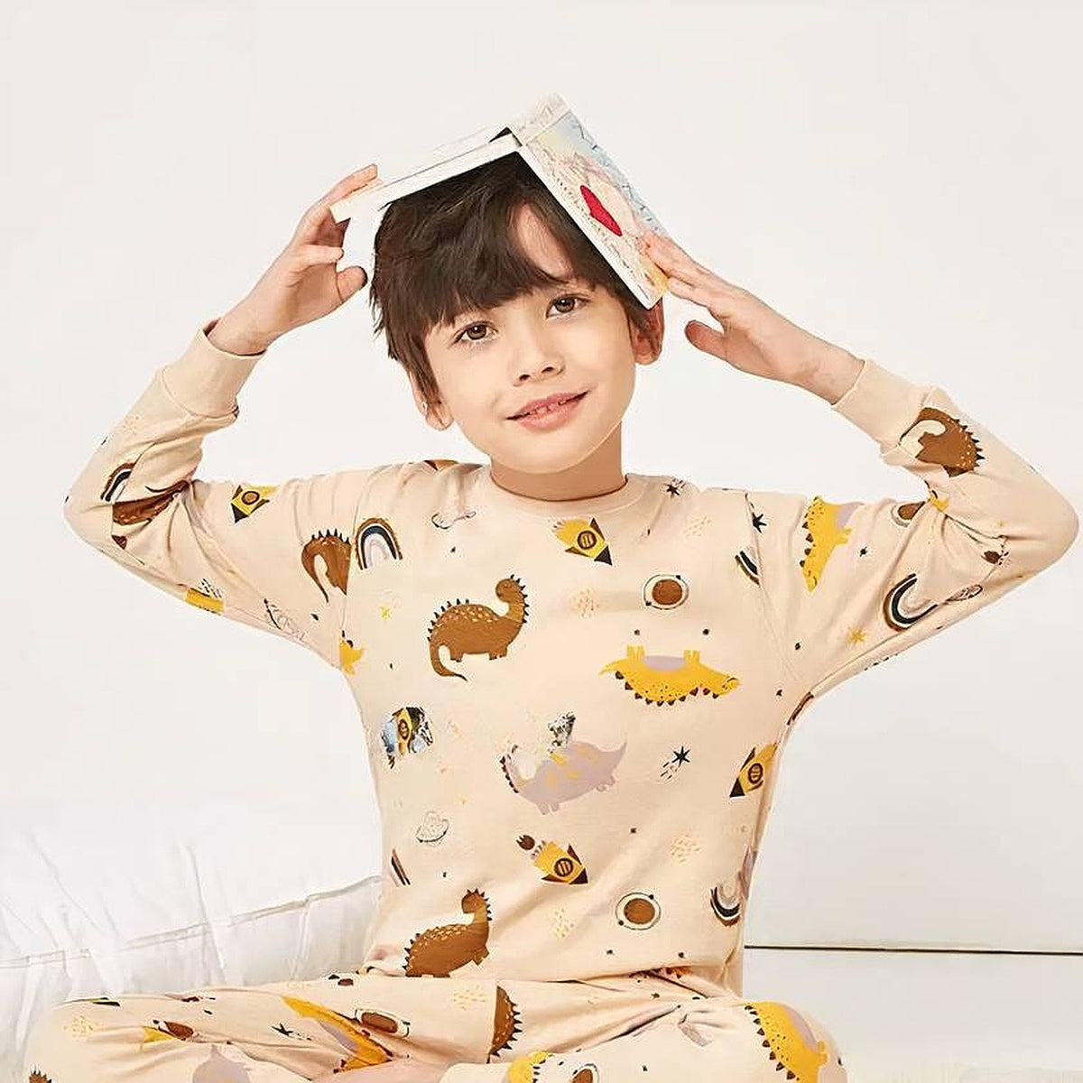 Garcon jouant avec un livre en pyjama dinosaures beige Image