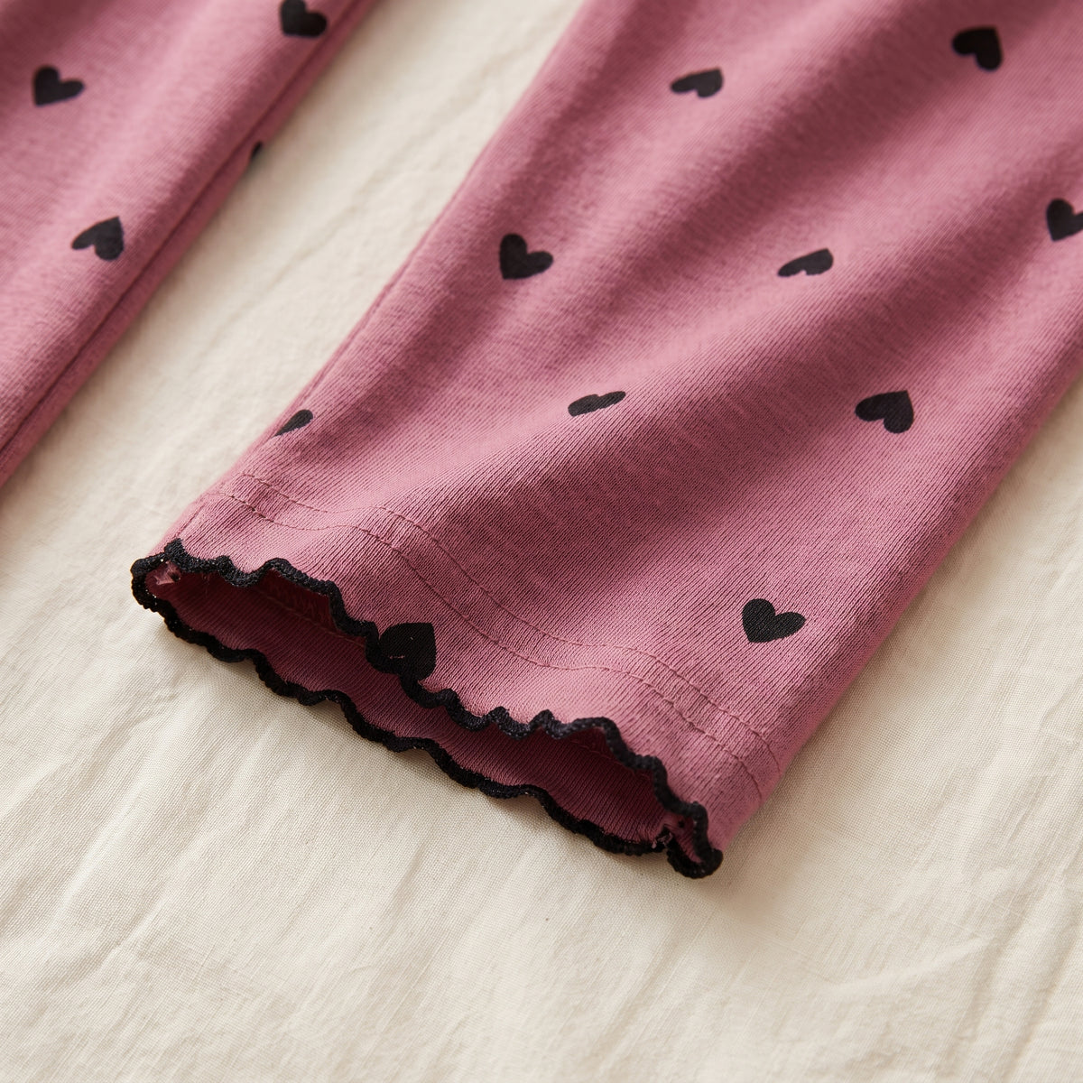 Bas de manche de la chemise de nuit vieux rose posé à plat, liseré noir ondulé et petits cœurs imprimés
