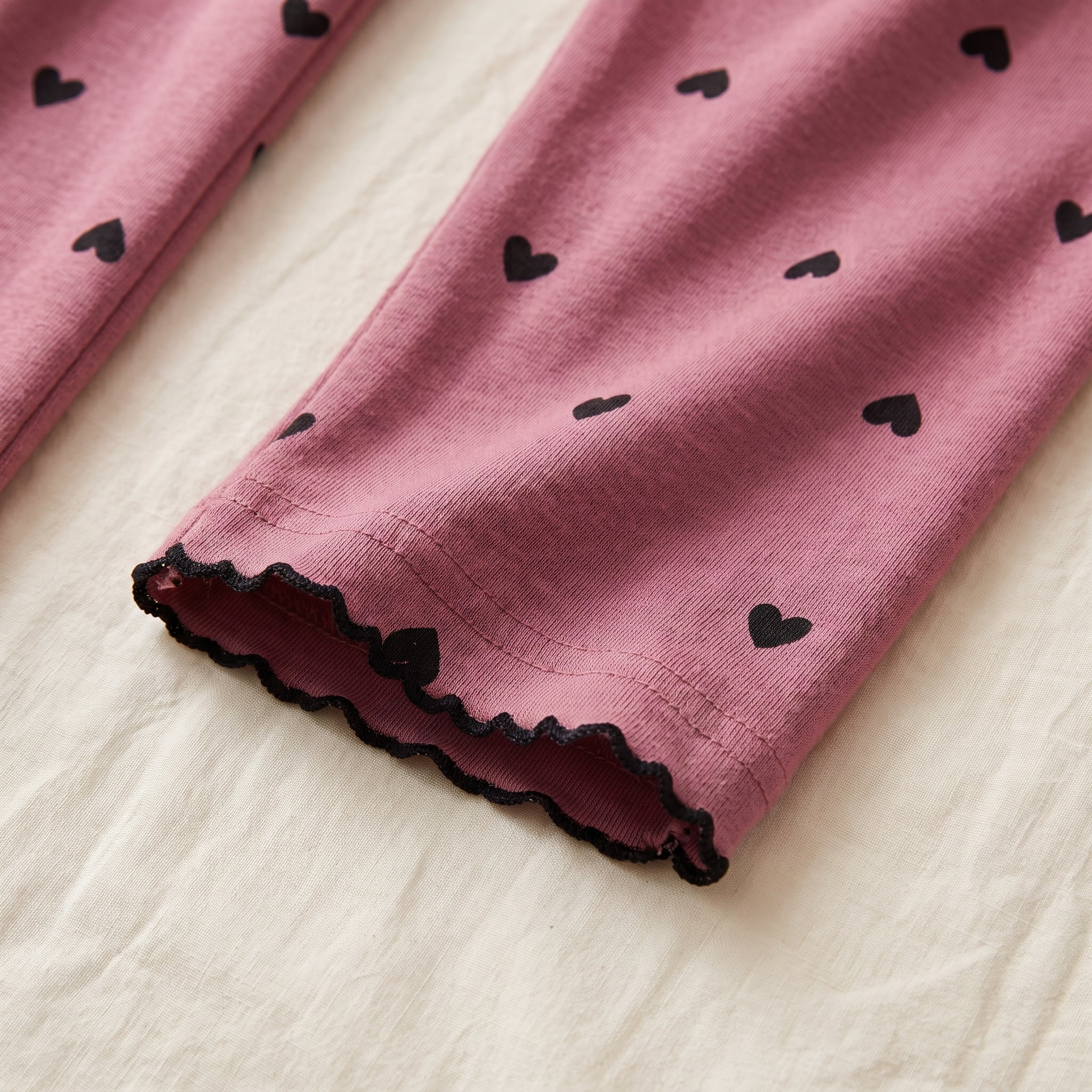 Bas de manche de la chemise de nuit vieux rose posé à plat, liseré noir ondulé et petits cœurs imprimés Image