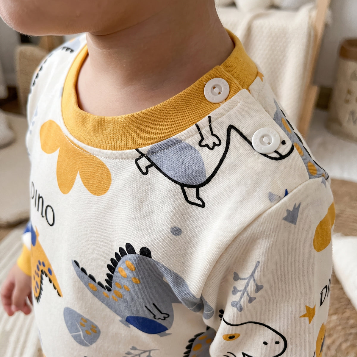 Encolure du pyjama dinosaures vue de près, côte jaune moutarde et deux pressions blanches à l’épaule