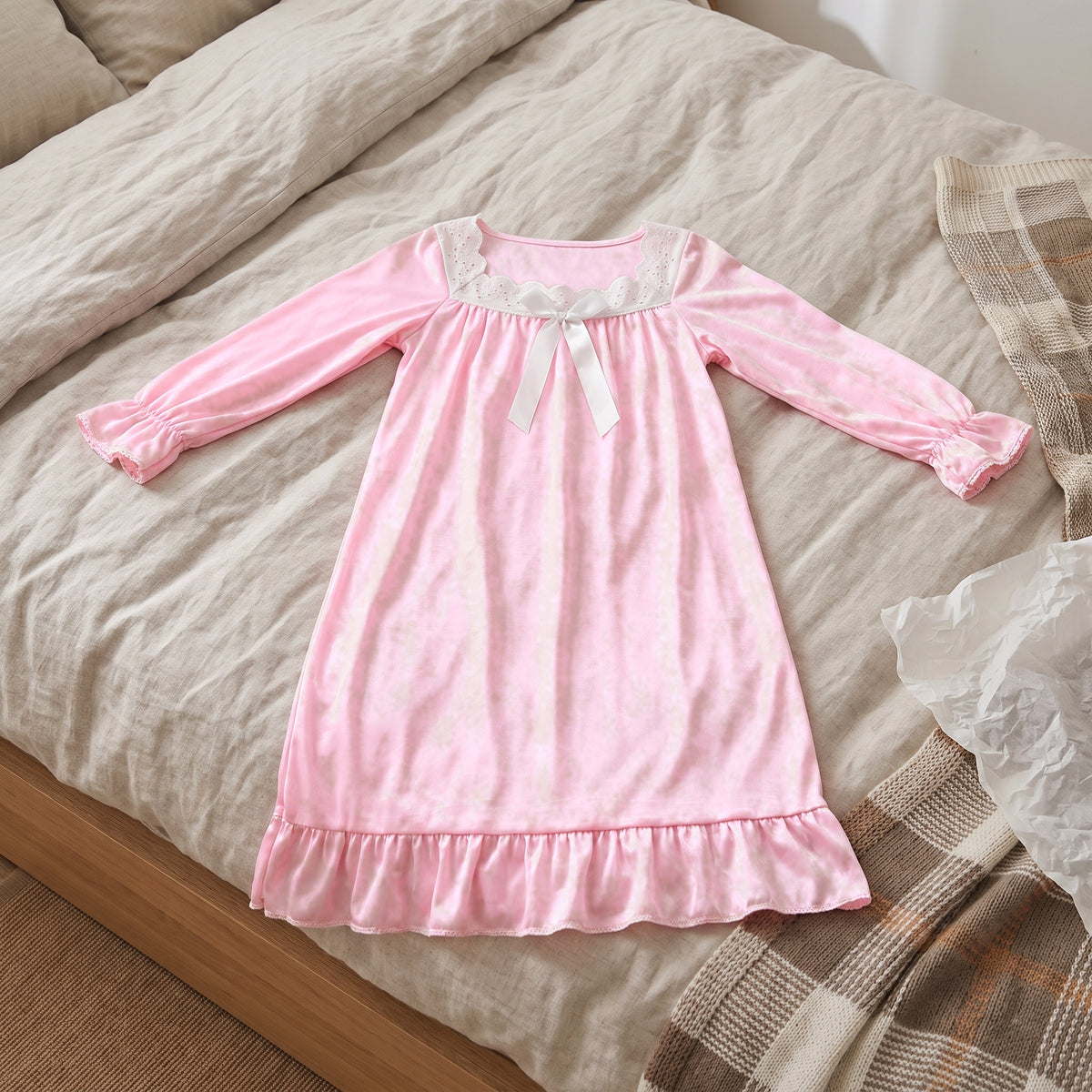 Chemise de nuit rose poudré pour petite fille étalée sur un lit, manches ouvertes, poignets froncés et volant de l’ourlet visibles