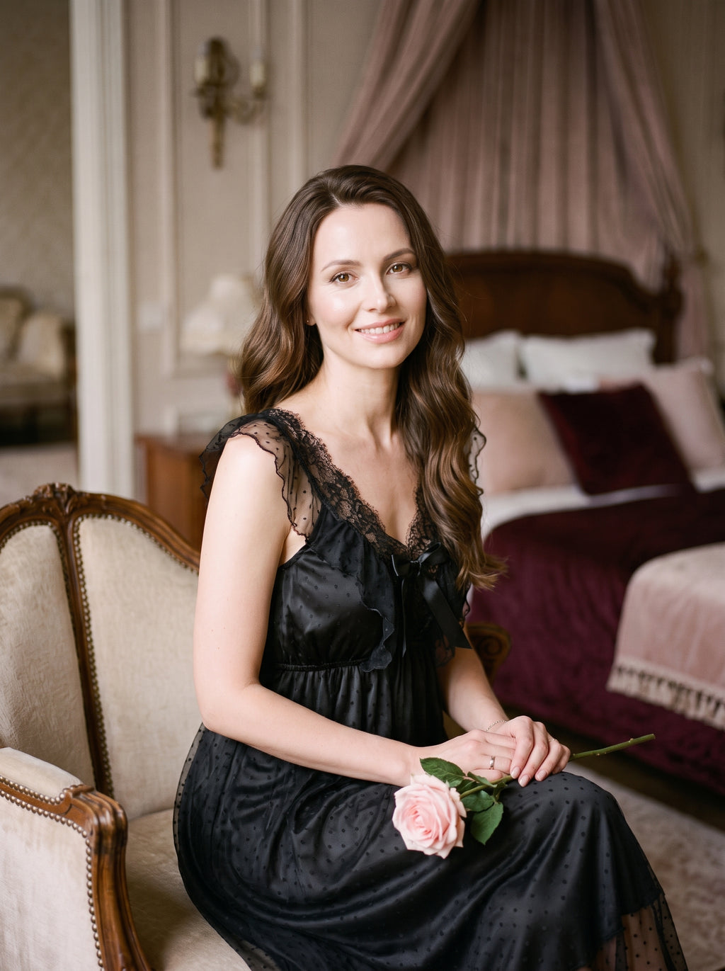 Femme brune souriante portant la chemise de nuit noire en satin et dentelle, assise dans un boudoir romantique