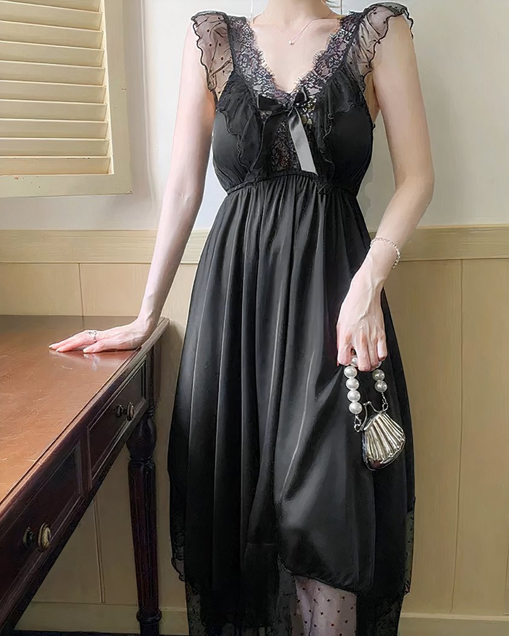 Chemise de nuit noire portée debout près d'un meuble ancien, tombé fluide du satin