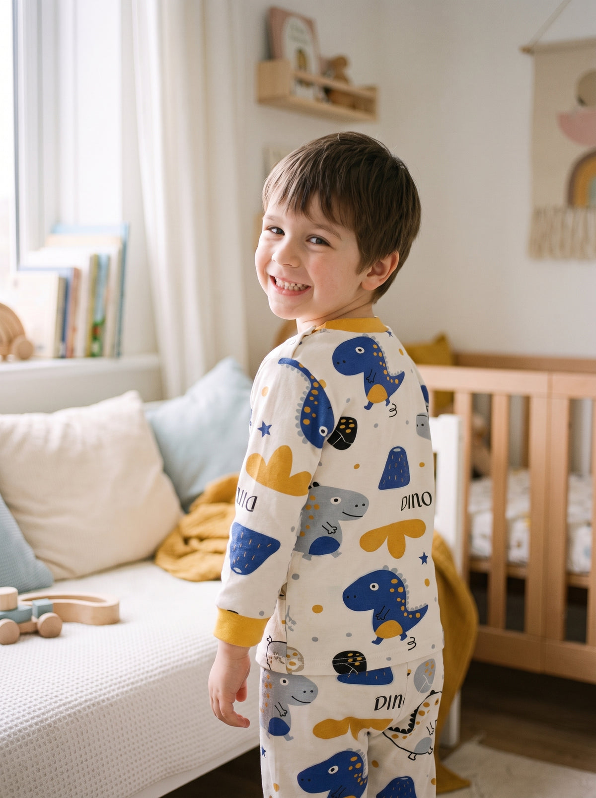 Petit garçon en pyjama imprimé dinosaures vu de trois-quarts dos, la tête tournée vers l’objectif