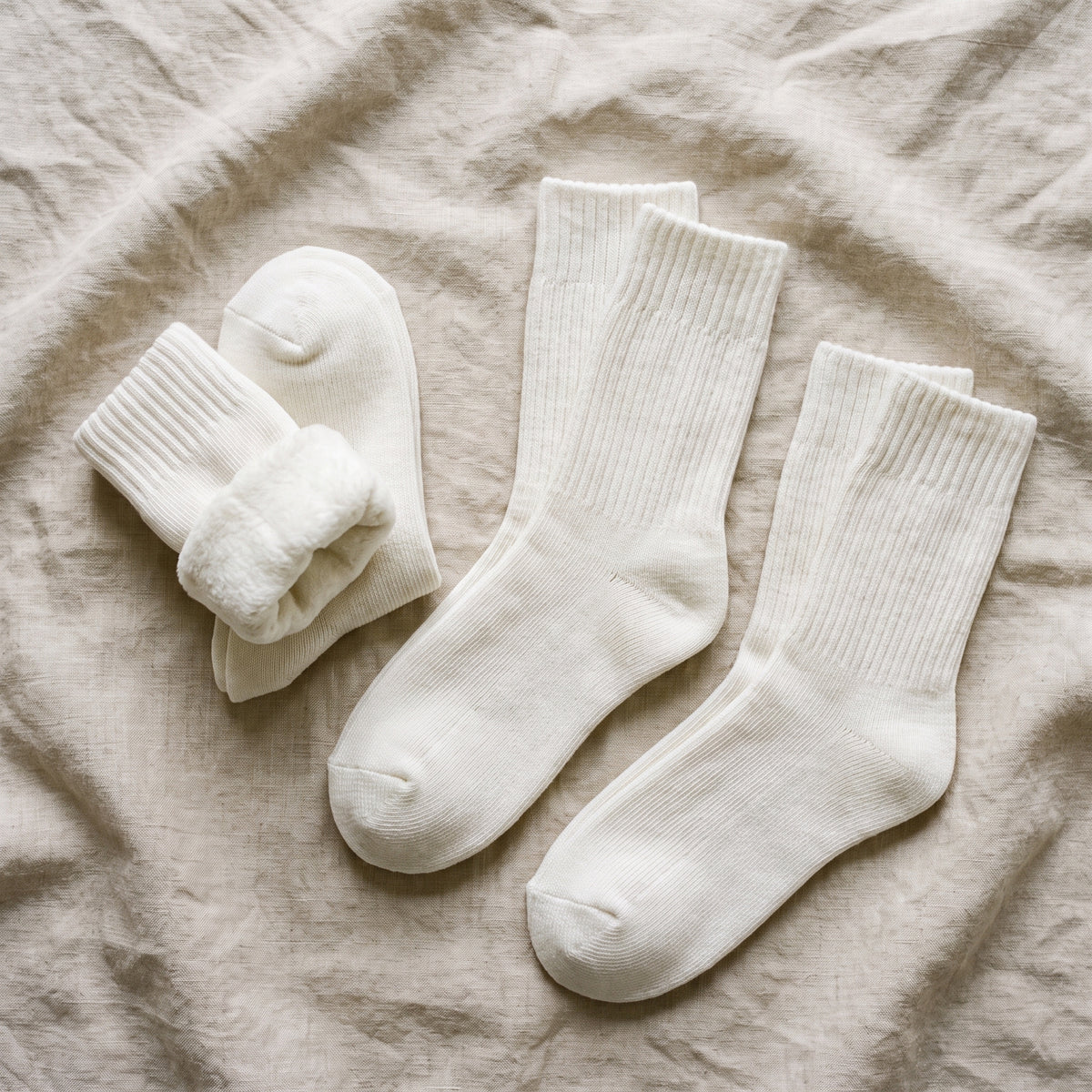 Lot de trois paires completes de chaussettes cocooning blanches disposees sur un linge en lin beige