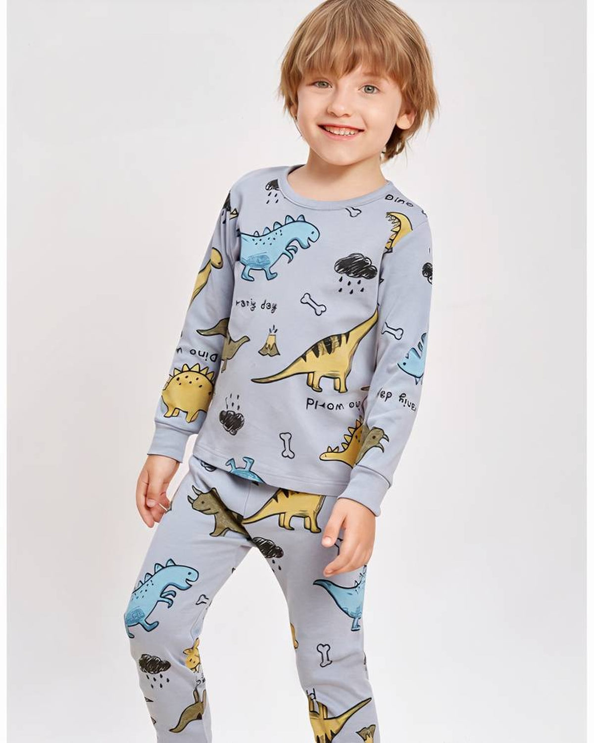 Garcon debout en pyjama dinosaures bleu-gris, motifs colores