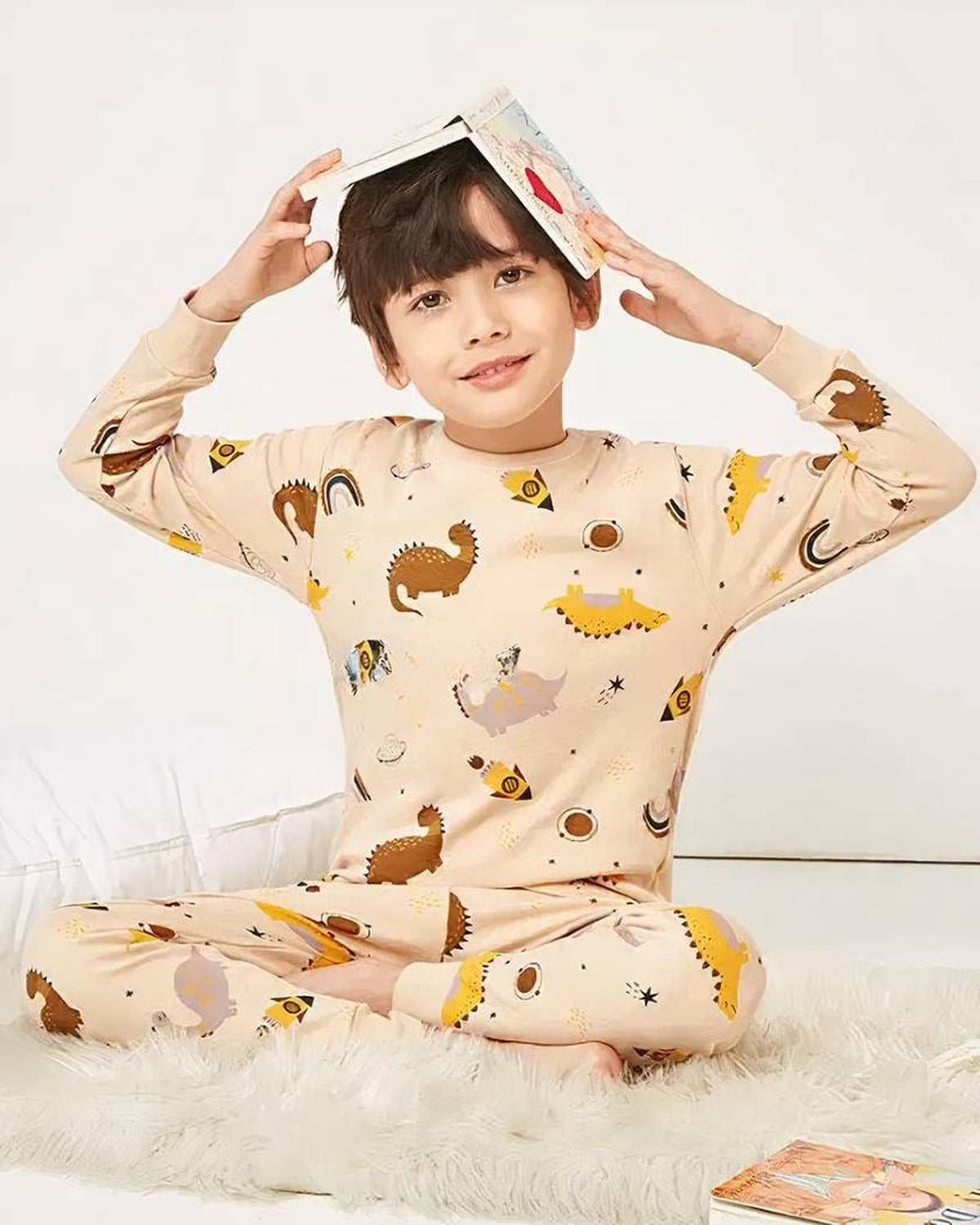 Garcon jouant avec un livre en pyjama dinosaures beige theme espace