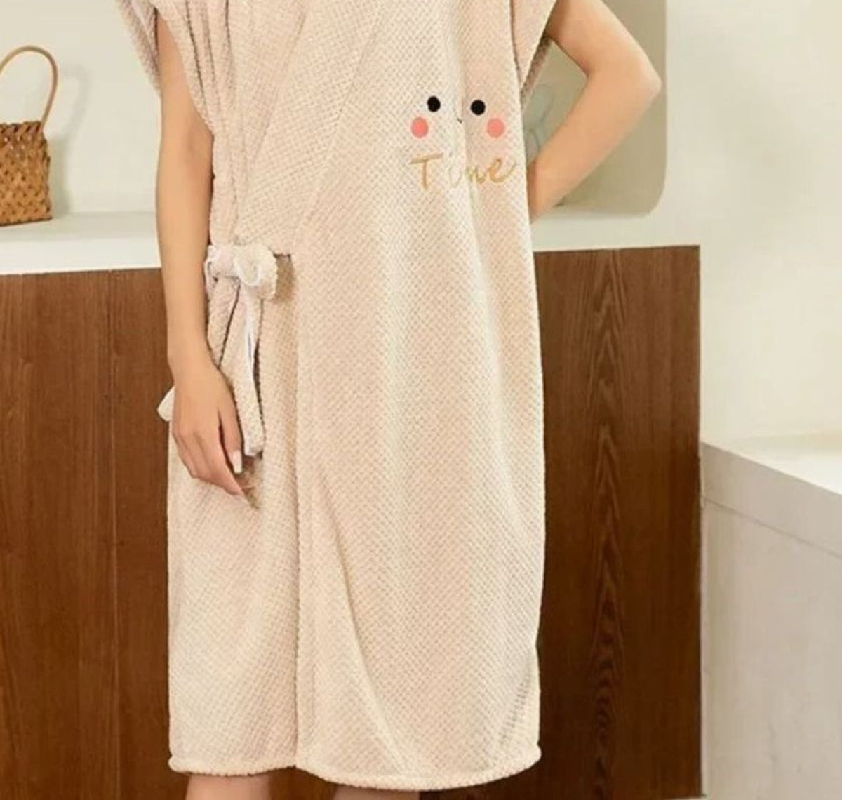 Plan rapproché du peignoir beige porté : la croisure, la ceinture nouée sur la hanche et la broderie à joues roses
