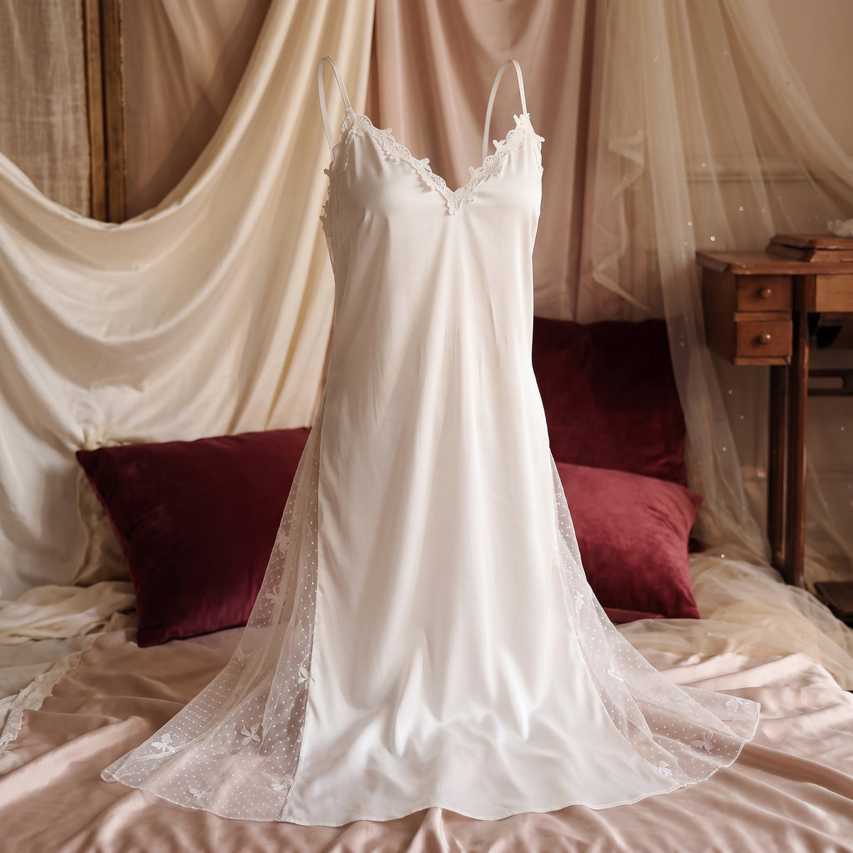 Nuisette blanche presentee de face sur mannequin invisible, decor boudoir aux coussins bordeaux