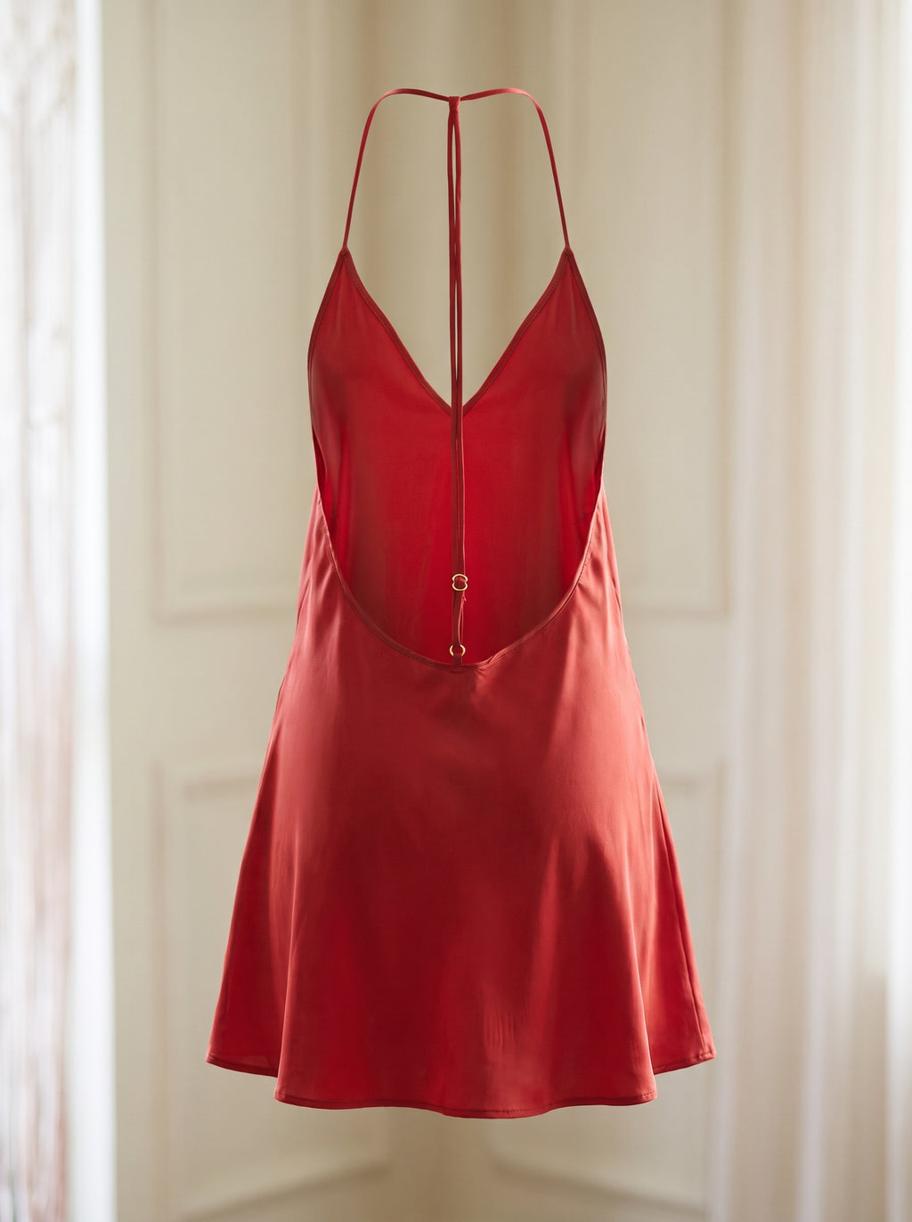 Nuisette rouge satinée vue de dos sur mannequin invisible, lien dorsal et ses deux anneaux de réglage, col en V visible par l’ouverture
