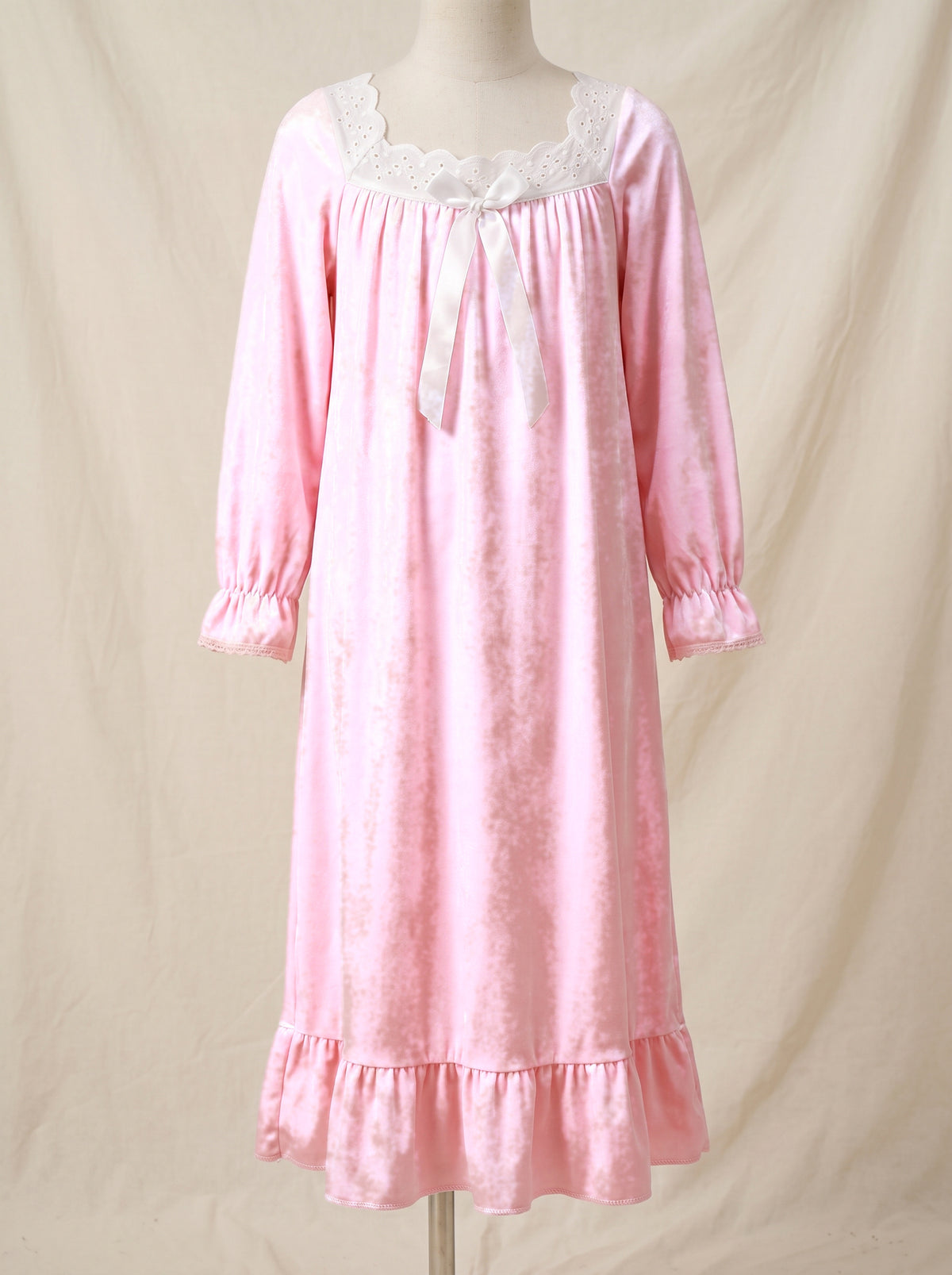 Chemise de nuit rose poudré pour petite fille présentée sur mannequin, col festonné, ruban de satin noué, manches froncées au poignet et ourlet à volant