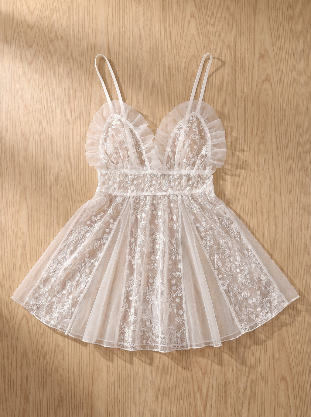 Nuisette babydoll en tulle brodé blanc à plat sur du bois clair, transparence visible