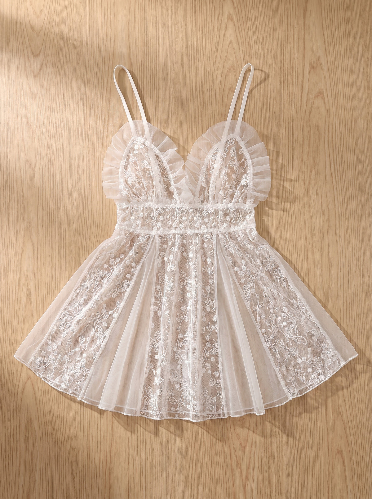 Nuisette babydoll en tulle brodé blanc à plat sur du bois clair, transparence visible