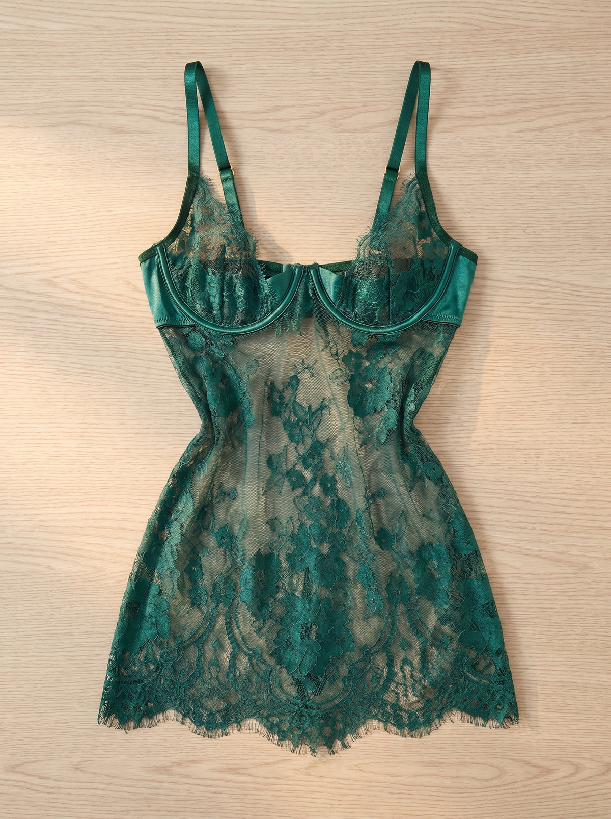 Nuisette courte en dentelle vert émeraude à plat sur du bois, armatures bordées de satin et ourlet en cils