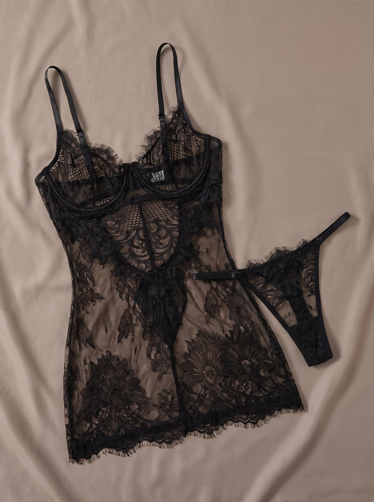 Nuisette babydoll noire en dentelle transparente posée à plat, avec string