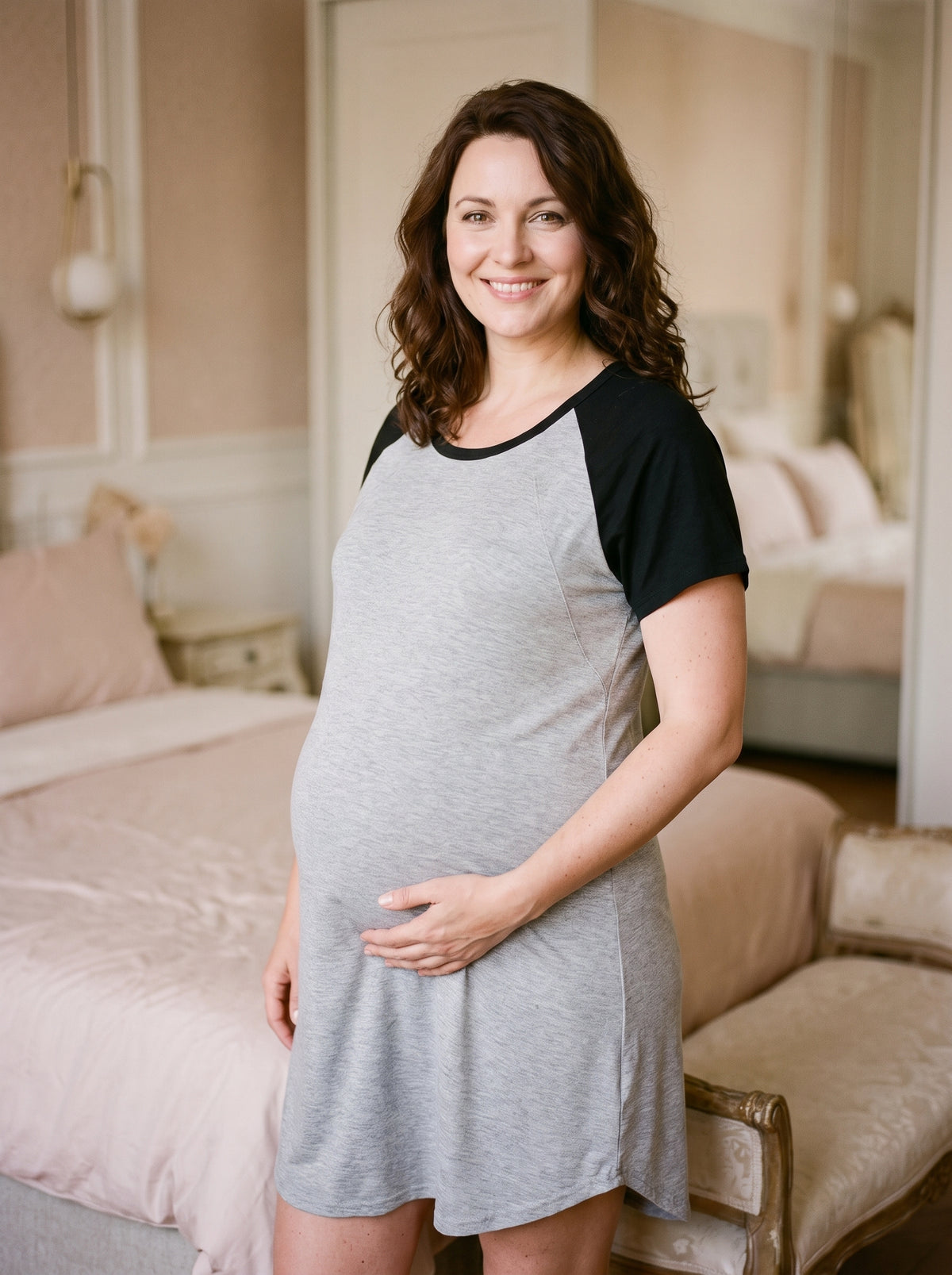 Femme enceinte en chemise de nuit de maternité gris chiné à manches raglan noires, debout dans une chambre