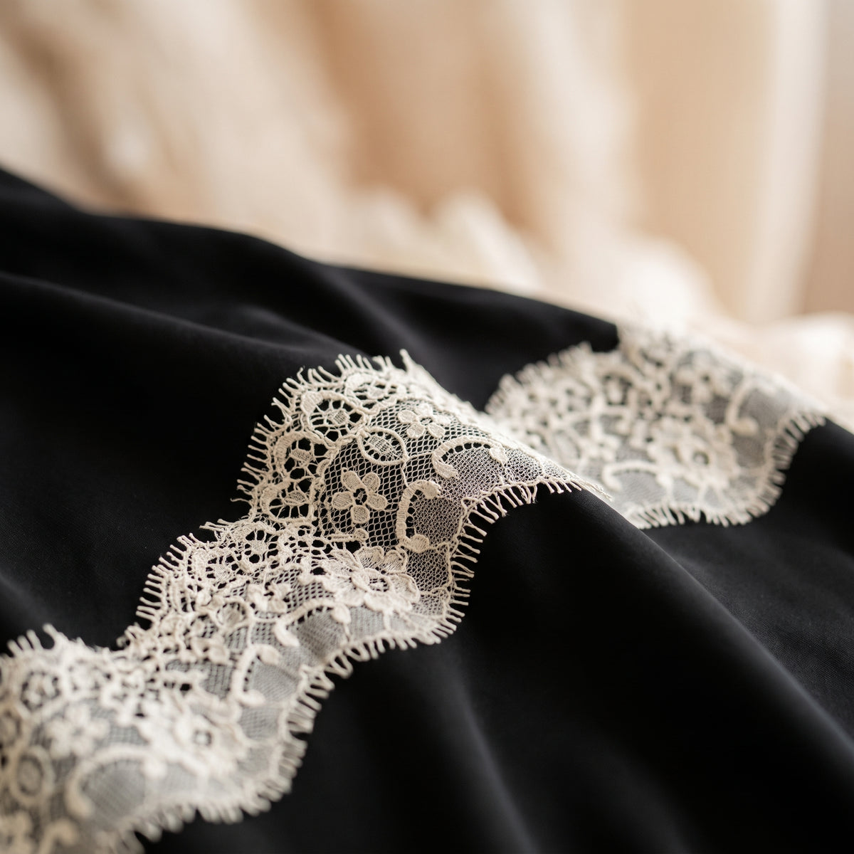 Gros plan sur la dentelle ivoire ajouree et le tissu noir fluide, detail de la matiere