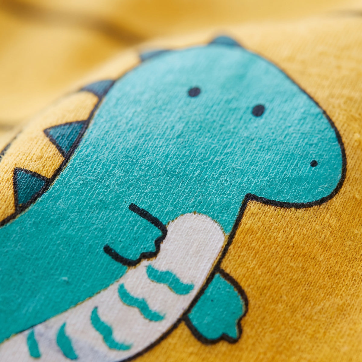 Gros plan sur le dinosaure imprimé sur le haut jaune rayé du pyjama