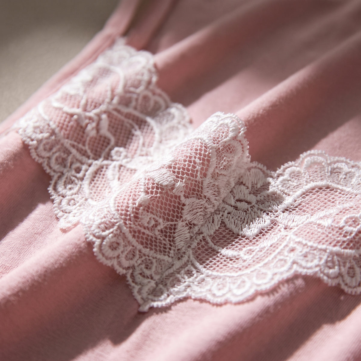 Gros plan macro sur la dentelle blanche festonnee de la nuisette rose poudre